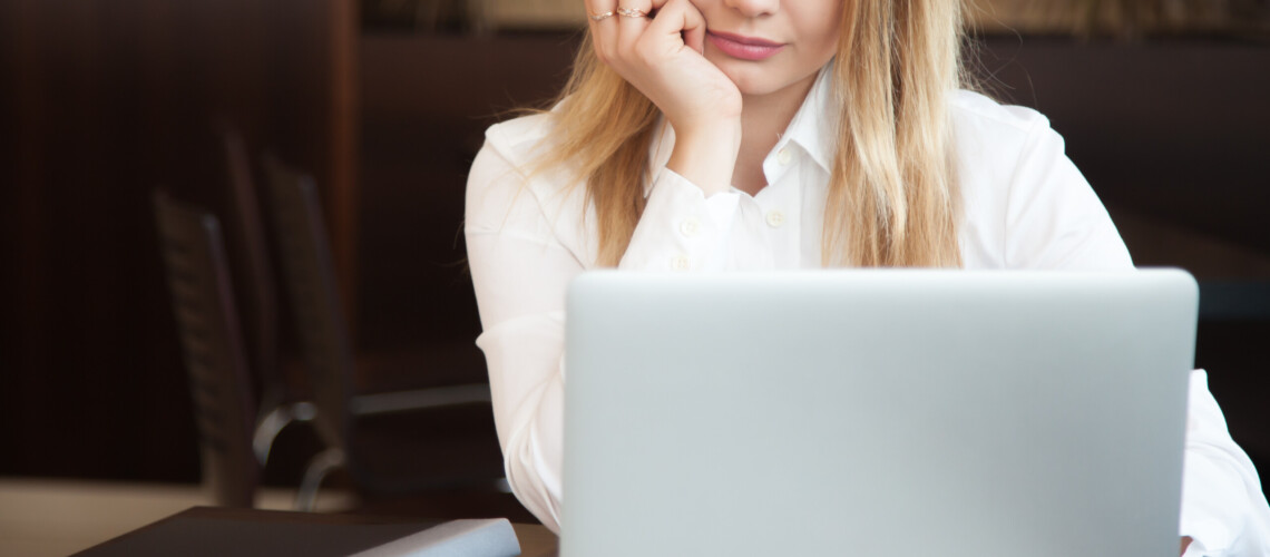 Young beautiful blond caucasian business woman working on laptop with concentrated, serious expression, cell phone and black dossier lying on the table